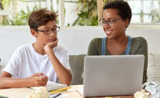 Self education and e learning concept. Satisfied black female volunteer tries to explain her strategy to young learner, watch attentively video in laptop computer. Tutor teaches skilled student